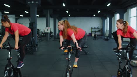Group-athletic-girls-performing-aerobic-riding-training-exercises-on-cycling-stationary-bike-in-gym