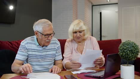 Stressed-senior-couple-discuss-unpaid-bank-debt-holding-bills,-doing-paperwork,-planning-budget