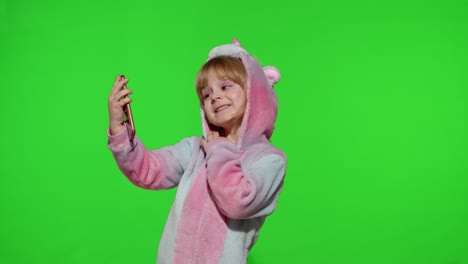 Child-girl-in-unicorn-costume-pajamas-using-smartphone,-kid-emotionally-makes-selfie-on-mobile-phone