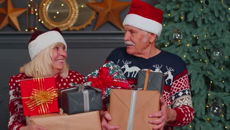 Senior-couple-family-in-Santa-Claus-hats-celebrating-looking-at-camera-holding-Christmas-gift-boxes