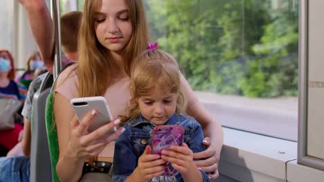 Child-girl-with-mother-using-smartphone-chatting-texting-in-social-media,-public-transport-bus,-tram