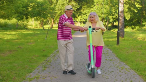 Senior-old-stylish-tourists-grandmother,-grandfather-using-electric-scooter-while-riding-in-park