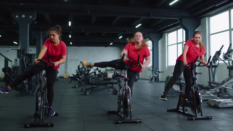 Group-of-smiling-friends-women-class-exercising,-training,-spinning-on-stationary-bike-at-modern-gym