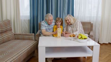 Älteres-Paar,-Großeltern-Und-Enkelin,-Genießen-Brettspiel-Bauturm-Aus-Bauklötzen-Zu-Hause