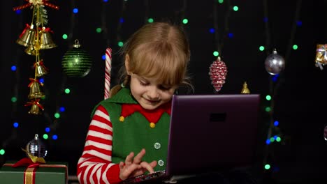 Kid-girl-in-Christmas-elf-costume-doing-shopping-online-using-laptop,-browsing-on-social-media