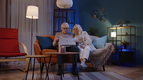 Happy-senior-old-couple-using-laptop-pc-talking-reading-discussing-internet-computer-news-at-home
