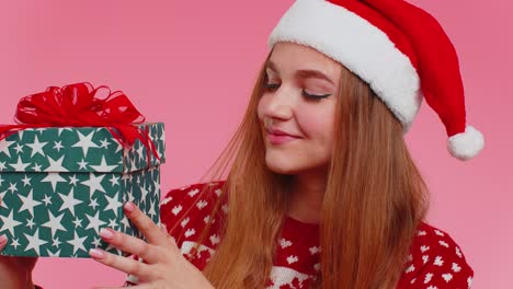Cheerful-lovely-girl-in-sweater-Santa-hat-presenting-one-Christmas-box,-excited-by-holiday-gift