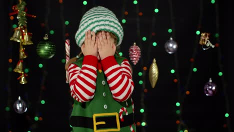 kid-girl-in-Christmas-elf-Santa-Claus-helper-costume-cover-face-with-hands-and-plays-hide-and-seek