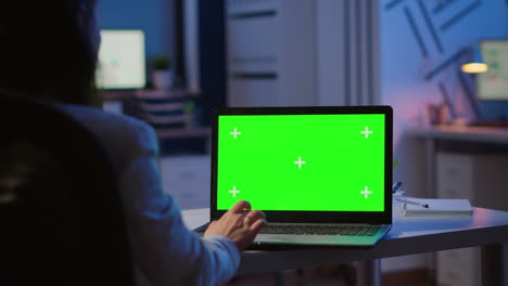 Woman-looking-at-laptop-with-green-mockup-during-night-time