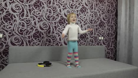 Little-happy-child-jumping-and-dancing-on-sofa-and-listening-music