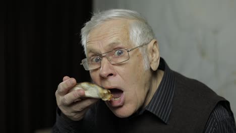 Beautiful-elderly-man-in-glasses-eats-pizza.-Shows-how-tasty-the-pizza-is.