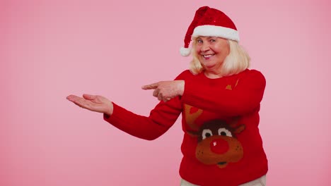 Großmutter-Im-Weihnachtspullover-Mit-Dem-Weihnachtsmann-Zeigt-Daumen-Nach-Oben-Und-Zeigt-Auf-Einen-Leeren-Platz,-Werbefläche