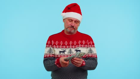 Reicher-Geschäftsmann-Im-Weihnachtspullover-Hält-Einen-Stapel-Geld-In-Dollar-Bargeld-Und-überlegt,-Welches-Geschenk-Er-Kaufen-Soll
