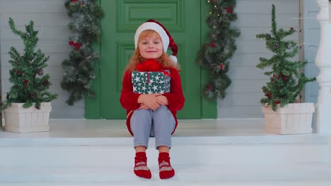 Fröhliches-Lächeln-Kleinkind-Kind-Mädchen-Kind-Sitzt-Auf-Dekorierten-Haus-Veranda-Hält-Eine-Weihnachtsbox