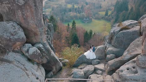 Newlyweds-stand-on-a-high-slope-of-the-mountain.-Groom-and-bride.-Arial-view