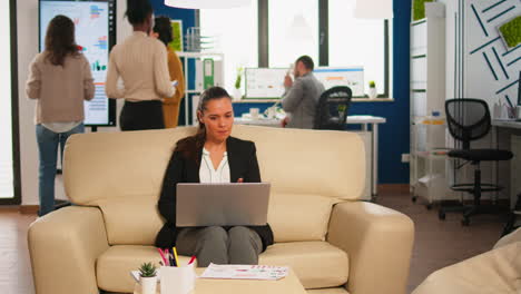 Manager-woman-holding-laptop,-looking-on-internet-while-sitting-on-couch-smiling