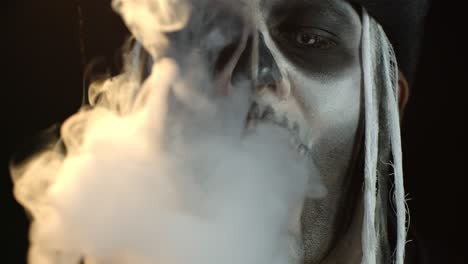 Nahaufnahme-Eines-Furchterregenden-Männergesichts-Mit-Gruseligem-Skelett-Halloween-Makeup,-Das-Zigarettenrauch-Ausatmet
