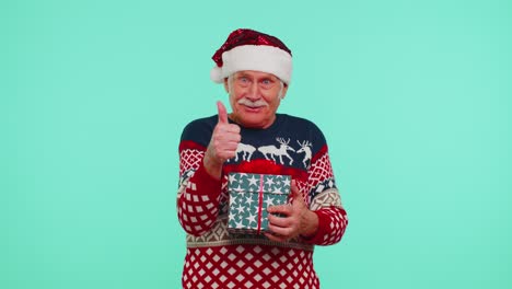 Grandfather-in-Santa-sweater-presenting-one-Christmas-gift-box,-stretches-out-his-hands-to-camera