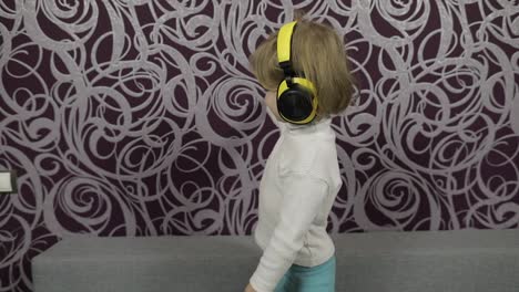 Little-happy-child-dancing-on-sofa-and-listening-music-in-headphones-at-home