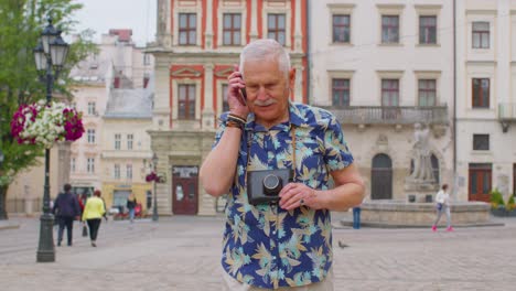 Älterer-Alter-Tourist-In-Stilvoller-Kleidung,-Der-Beim-Spazierengehen-Auf-Der-Stadtstraße-Mit-Dem-Mobiltelefon-Telefoniert