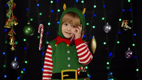 Kleines-Mädchen-Im-Weihnachtselfenkostüm-Als-Weihnachtsmannhelfer-Ruft-Auf-Dem-Handy-An-Und-Gratuliert
