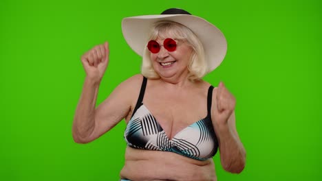 Mature-old-woman-traveler-in-red-sunglasses-and-hat-dancing,-celebrating,-smiling-on-chroma-key