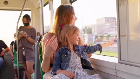 Family-rides-in-public-transport,-mother-with-little-daughter-sit-together-and-look-out-window-tram