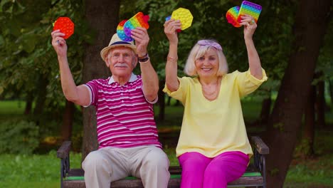 Stylish-senior-grandmother-grandfather-holding-squeezing-anti-stress-toy-simple-dimple-games-in-park