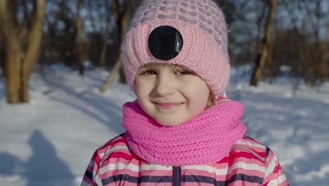 Joyful-little-child-girl-looking-at-camera,-smiling,-fooling-around,-making-faces-in-winter-park