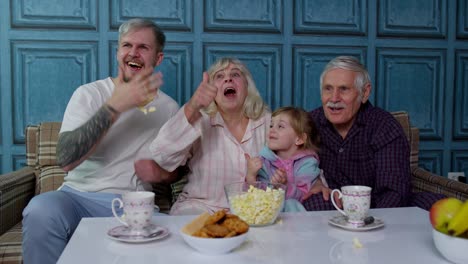 Multigenerational-happy-family-laughing,-watching-comedy-cartoons-television-movies,-eating-popcorn