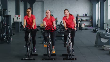 Un-Grupo-De-Chicas-Realiza-Una-Rutina-Cardiovascular-De-Entrenamiento-Aeróbico-En-Simuladores-De-Bicicletas,-Entrenamiento-En-Bicicleta.