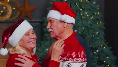 Älteres-Ehepaar-Mit-Weihnachtsmann-Hüten-Feiert-Weihnachten,-Blickt-In-Die-Kamera-Und-Umarmt-Sich-Zu-Hause