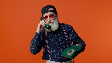 Senior-bearded-gray-haired-man-talking-on-wired-vintage-telephone-of-80s,-says-hey-you-call-me-back