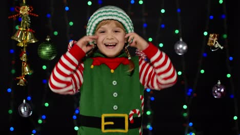 Kleines-Mädchen-Im-Weihnachtselfenkostüm-Des-Weihnachtsmanns-Lacht-Fröhlich-Auf-Dem-Hintergrund-Mit-Girlanden