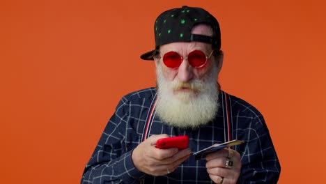 Senior-old-stylish-bearded-man-using-credit-bank-card-and-smartphone-purchases-online-shopping