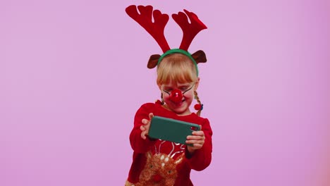 Toddler-girl-in-Christmas-deer-antlers-enthusiastically-playing-racing-video-games-on-mobile-phone