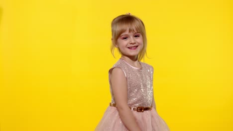 Little-smiling-blonde-child-kid-girl-waving-greeting,-hello-or-bye-with-hand-on-yellow-background