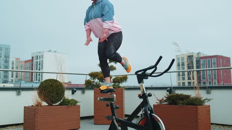 Sportliche-Frau-Führt-Akrobatisches-Training-Mit-Schwalbentricks-Auf-Einem-Stationären-Fahrrad-Durch