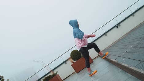 Sport-woman-in-sportswear-wears-hood-doing-workout,-step-cardio-exercising-training-on-roof-of-house