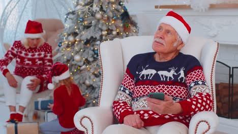 El-Anciano-Abuelo-Compra-Regalos-De-Navidad-Haciendo-Compras-En-Línea-En-Un-Teléfono-Inteligente-En-Casa