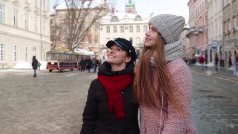 Dos-Mujeres-Turistas-Sonrientes-Caminando-Juntas-Por-Las-Calles-De-La-Ciudad,-Una-Pareja-Familiar-Hablando,-Abrazándose