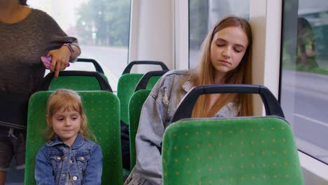 Exhausted-mother-fall-asleep-and-missed-stop-station-in-tram,-kid-daughter-wakes-tired-sleepy-woman