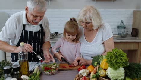 Senior-couple-in-kitchen-teaching-granddaughter-child-how-to-cook,-chopping-pepper-with-knife