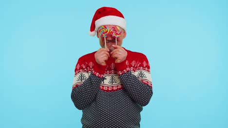 Funny-man-in-red-Christmas-sweater-holding-candy-striped-lollipops-hiding-behind-them-fooling-around