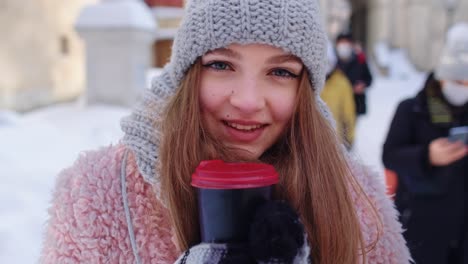Girl-tourist-with-hot-drink-in-cup-looking-around-through-street-in-town-during-holiday-vacations