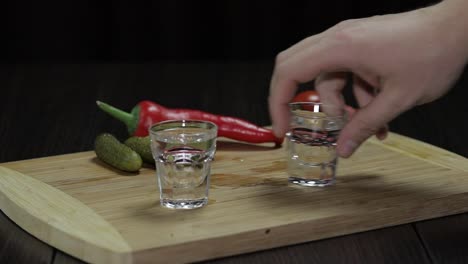 Man-takes-a-glass-filled-with-vodka-from-the-wooden-board