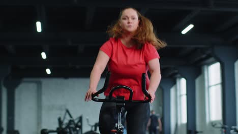 Sportliche-Frau,-Die-Im-Fitnessstudio-Auf-Einem-Stationären-Fahrrad-Fährt-Und-Gewicht-Verliert,-Während-Sie-Im-Innenbereich-Trainiert