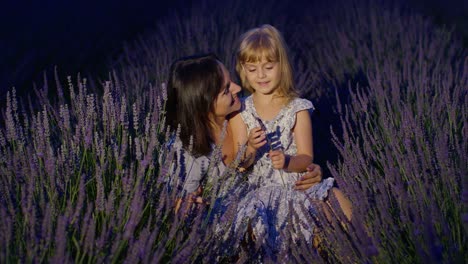 Mother-enjoying-time-with-child-daughter-girl,-touching-sniffing-aromatic-flowers-in-lavender-field