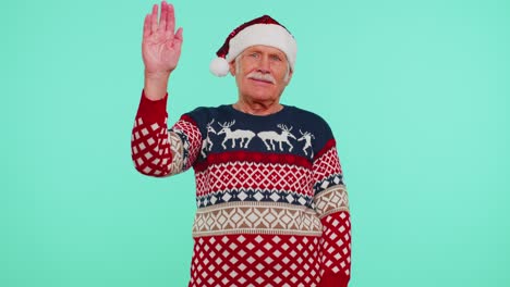 Grandfather-man-in-Christmas-sweater-with-deers-waves-hand-palm-in-hello-gesture-welcomes-someone