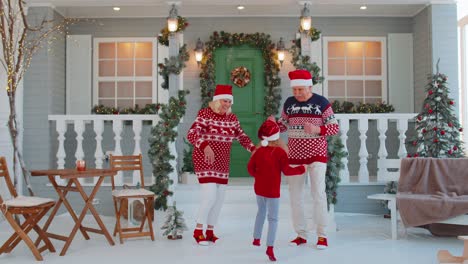 Cheerful-old-grandparents-with-granddaughter-child-kid-dancing-around-decorated-Christmas-house-tree